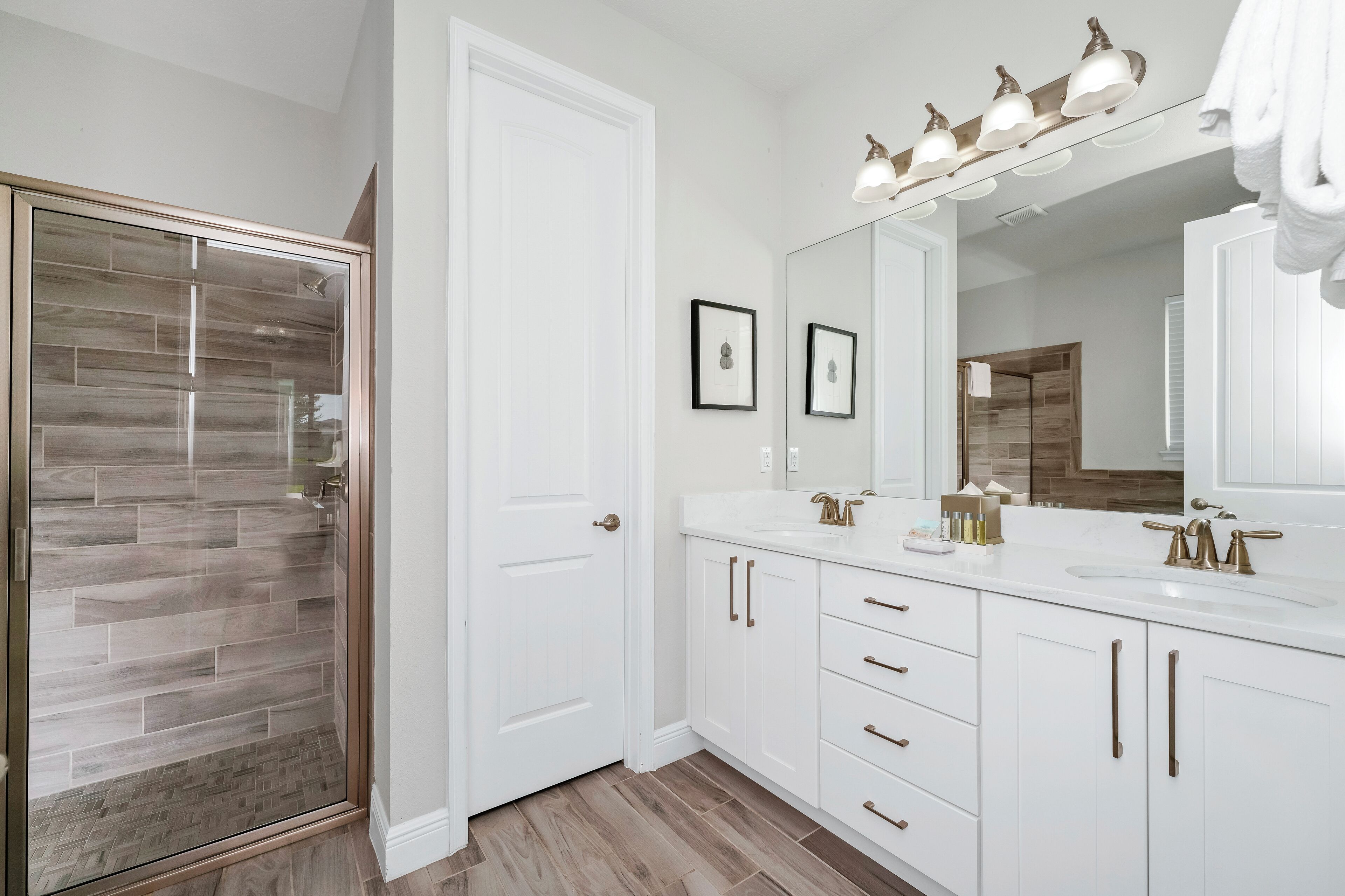 A modern bathroom with a glass shower enclosure, white cabinetry, and a large mirror with overhead lighting.