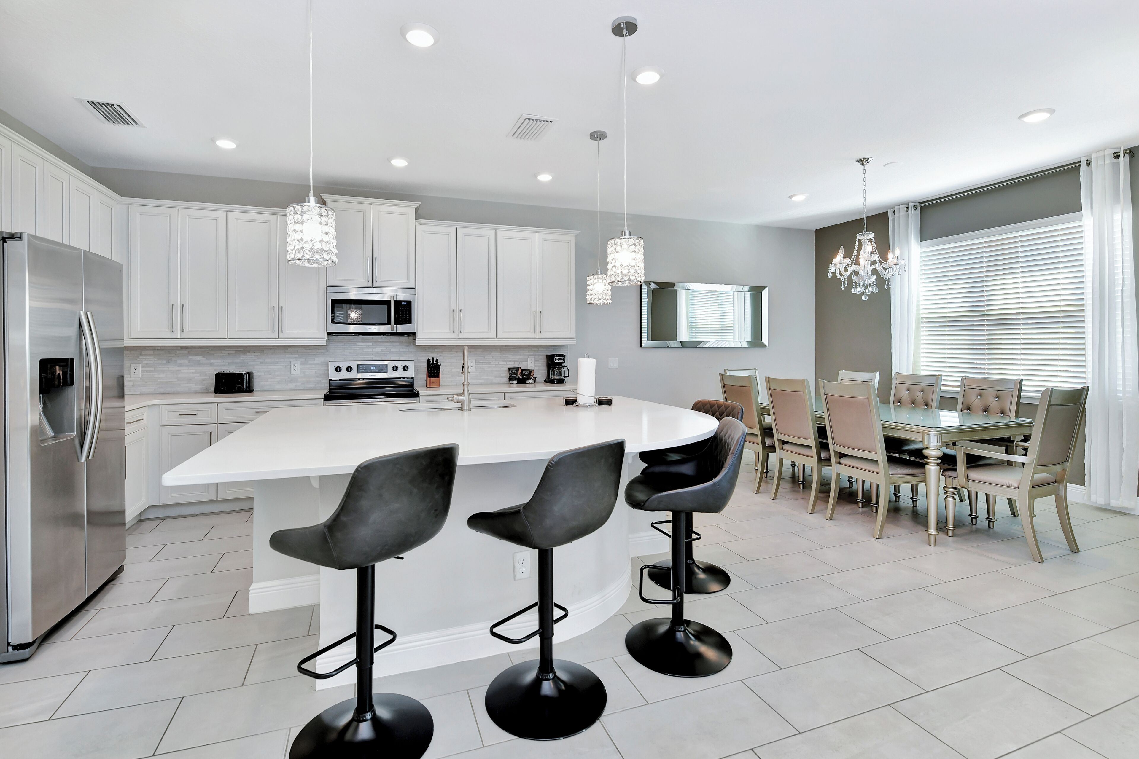 Una cocina moderna con gabinetes blancos, una isla central con taburetes de bar, electrodomésticos de acero inoxidable e iluminación colgante.