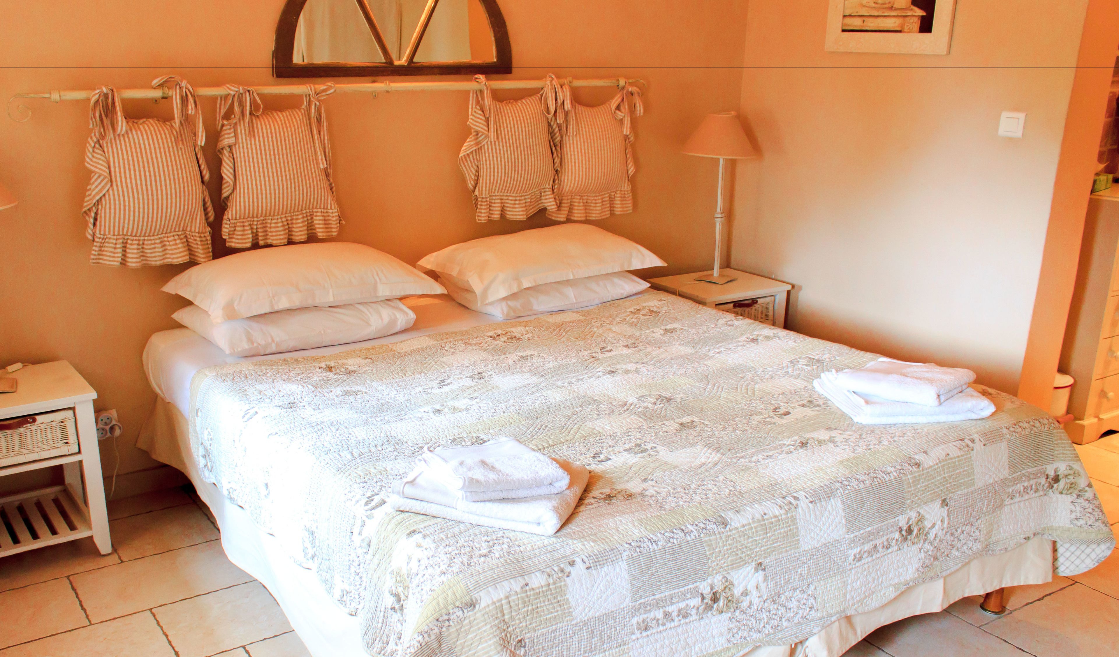 Uma cama bem arrumada com um cobre-leito estampado com flores, duas almofadas brancas e uma luminária de cabeceira.