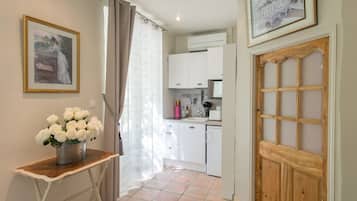 Un pasillo estrecho con una puerta de madera, un armario blanco, un lavamanos y una pequeña mesa con un florero.