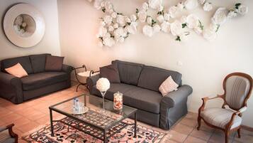 Ein Wohnzimmer mit zwei grauen Sofas, einem Glastisch, einem Holzstuhl und einer Wand, die mit weißen Rosen verziert ist.