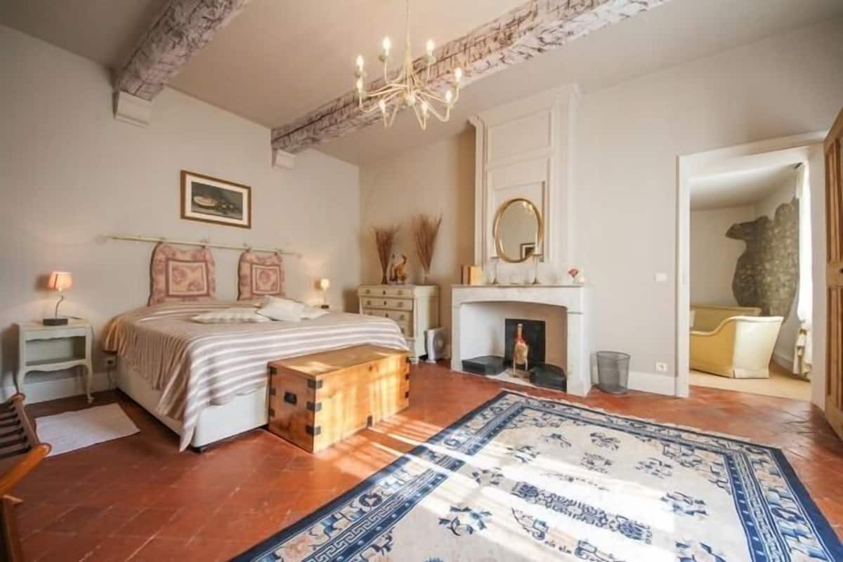 Un dormitorio con cama, mesitas de noche, cómoda, espejo, chimenea y una alfombra estampada.