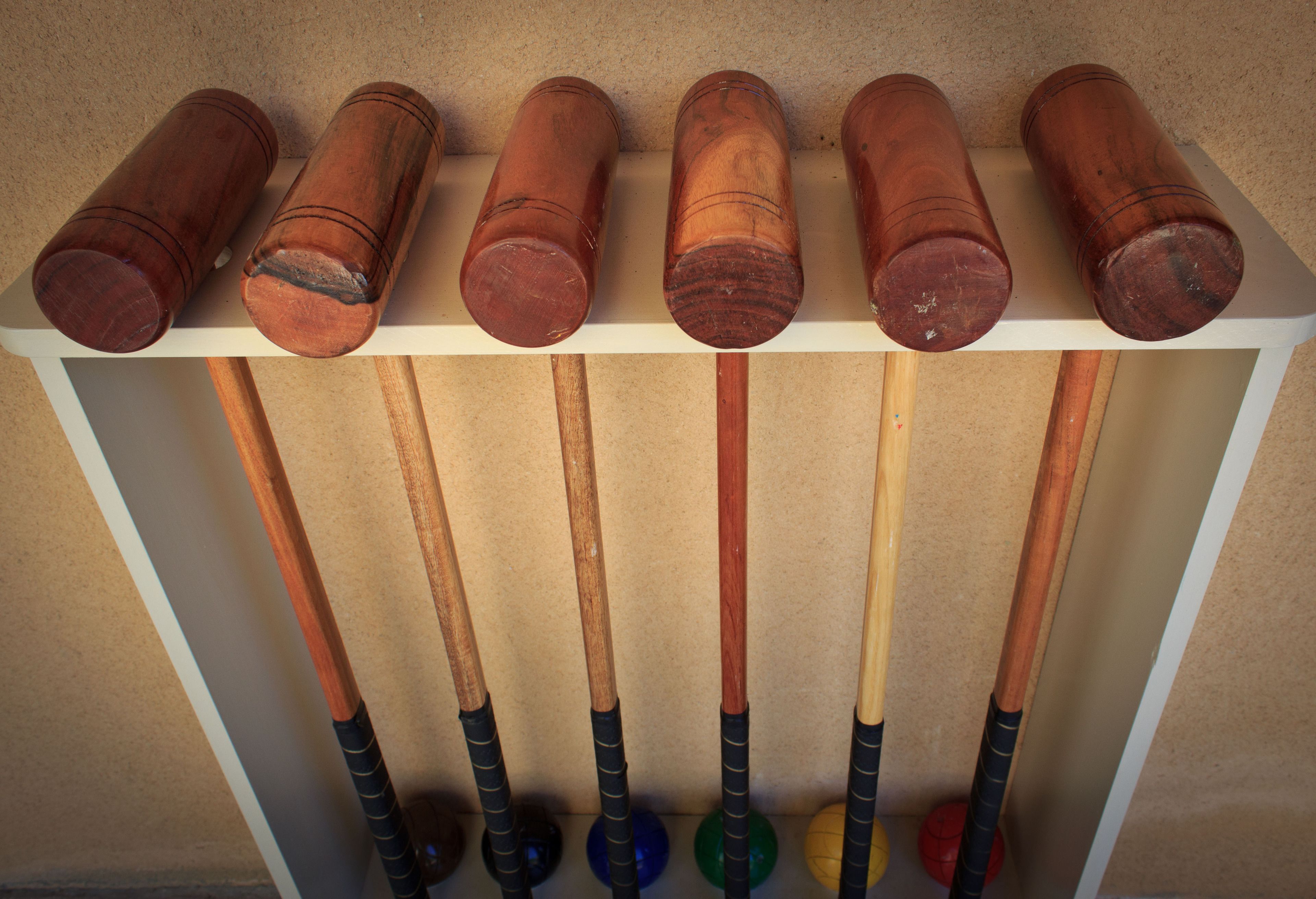 A rack of wooden pool cues with handles and balls at the bottom.