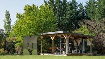 A gazebo with exercise equipment, surrounded by lush greenery and trees.