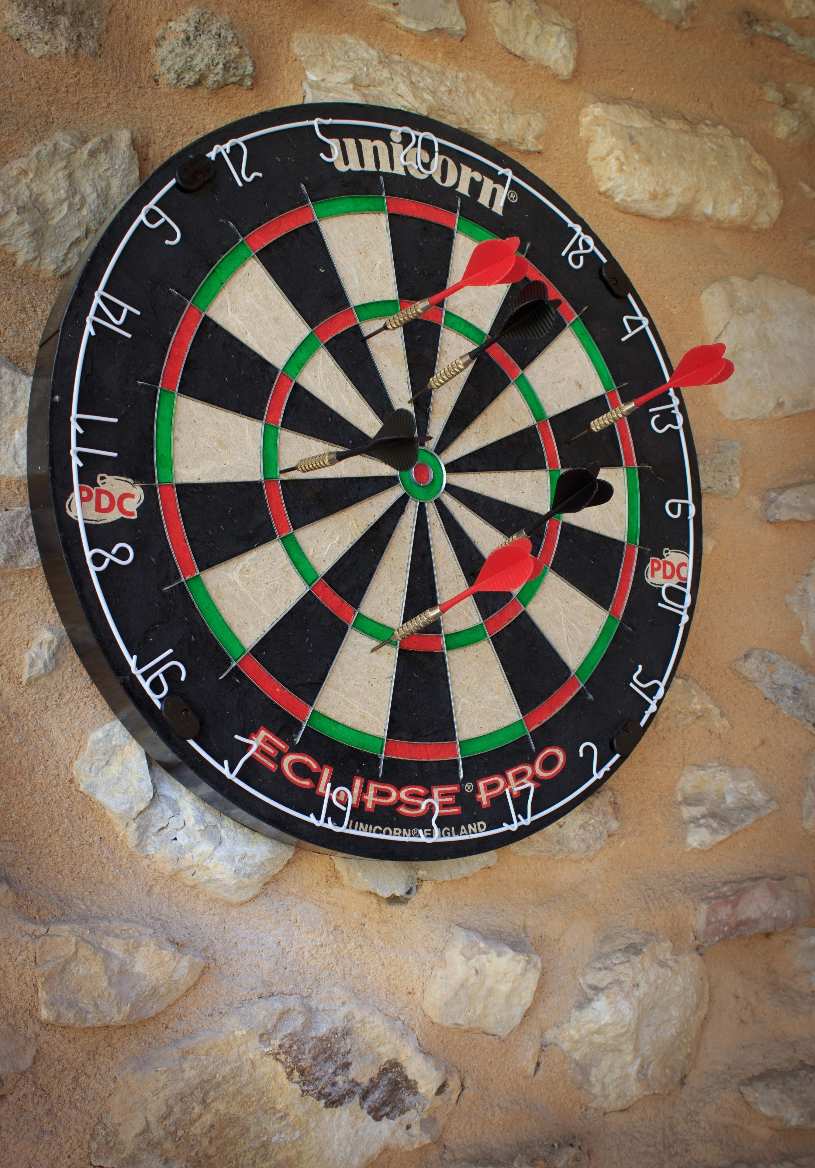 A dartboard with multiple darts stuck in it, placed on a stone wall.