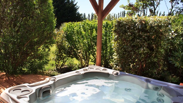 Un jacuzzi en un jardín con cubierta de madera y abundante vegetación.