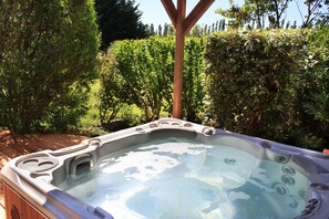 A hot tub in a garden with wooden decking and lush greenery. - Le Domaine des Carmes & Spa (Le Thor)