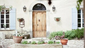 Un patio rústico con una puerta de madera, plantas en macetas y un banco de piedra.