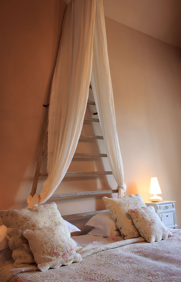 A bedroom with a canopy bed, a wooden ladder, a bedside lamp, and floral pillows.