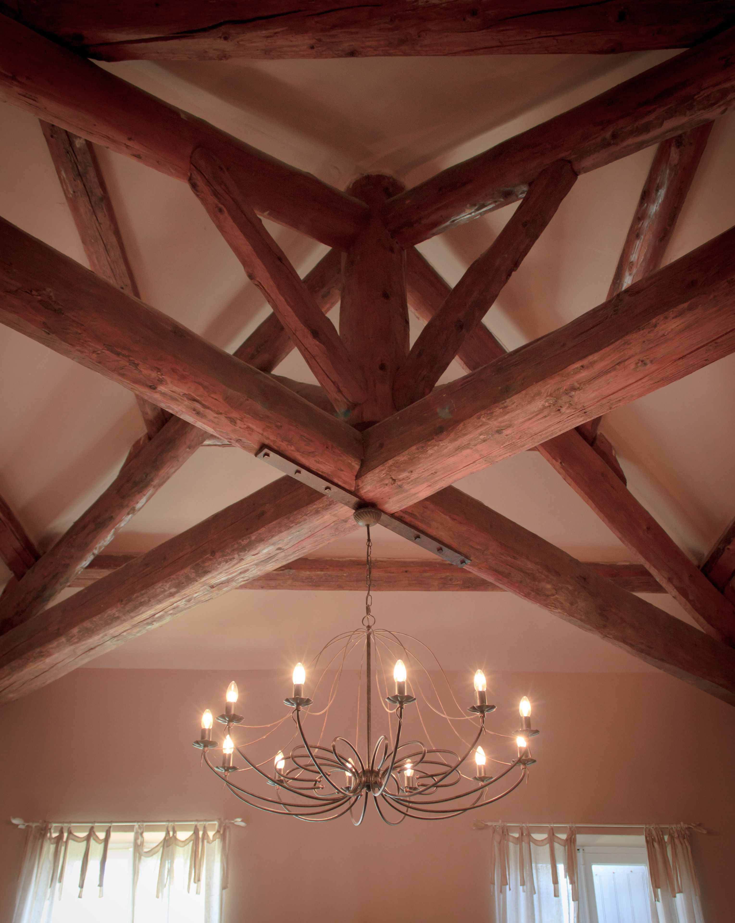 Una habitación con vigas de madera a la vista y una araña con numerosas velas.