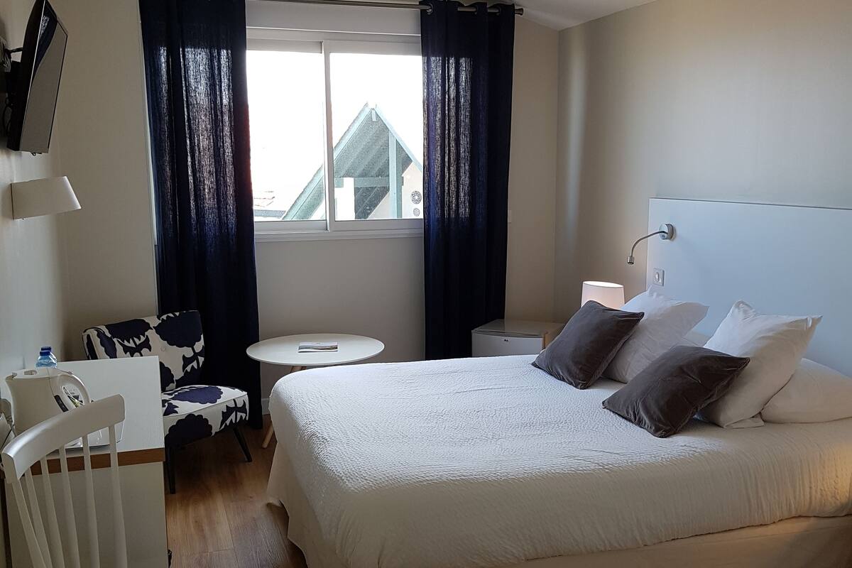 A hotel room with a bed, a desk, a chair, a TV, and a window with curtains.