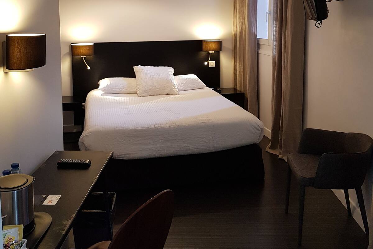 A hotel room with a large bed, bedside lamps, a TV, a desk with a remote control, and a chair.