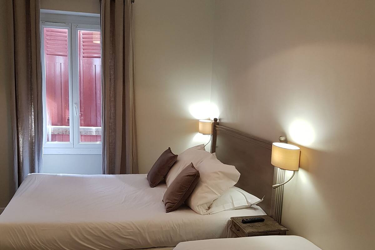 A double bed with a wooden headboard, two bedside lamps, and a window with curtains.