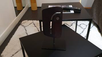 Una pequeña mesa negra con una silla frente a ella, un control remoto y dos botellas en el suelo.