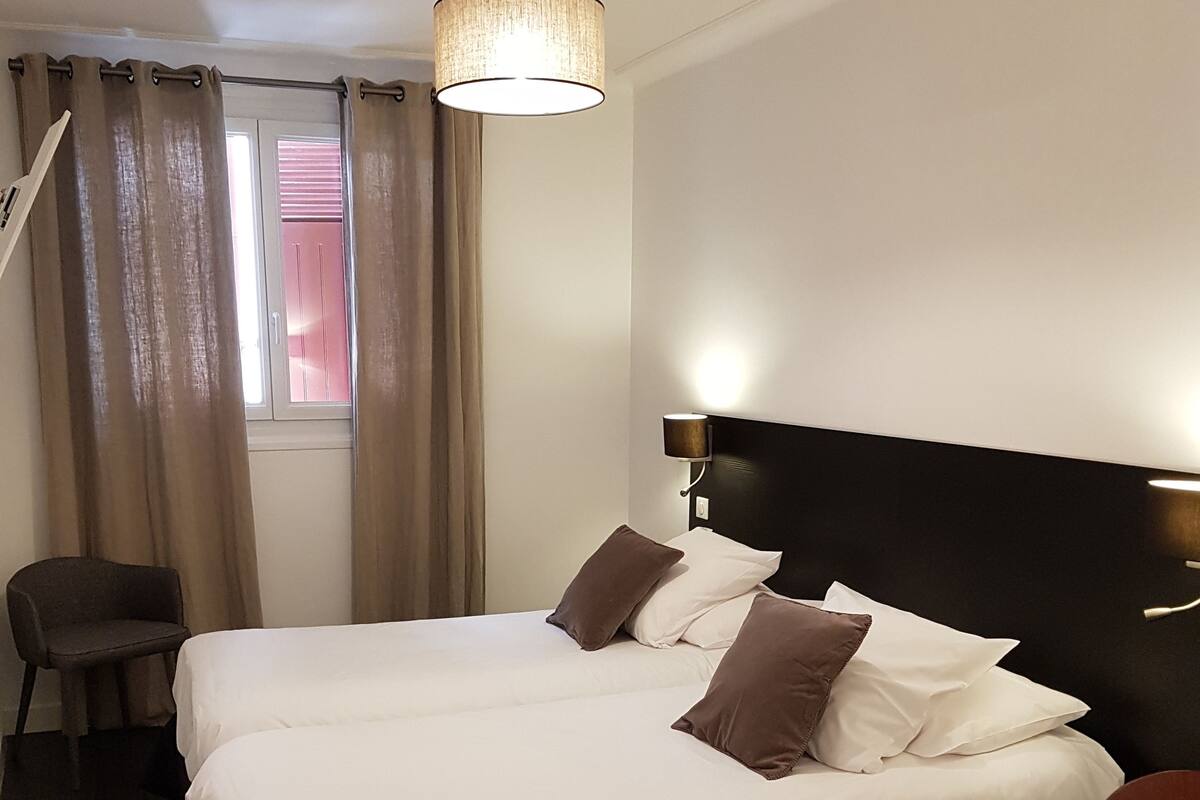 A hotel room with a large bed, a chair, a desk, and a window with curtains.