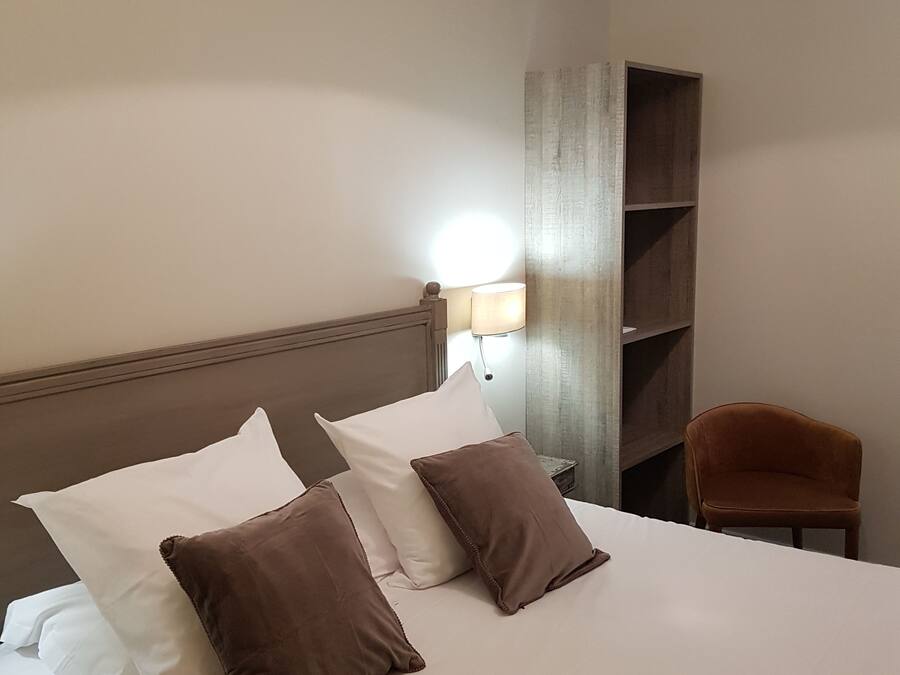 Une chambre d’hôtel comprenant un lit, des oreillers, une table de chevet, une lampe, une chaise et une étagère.
