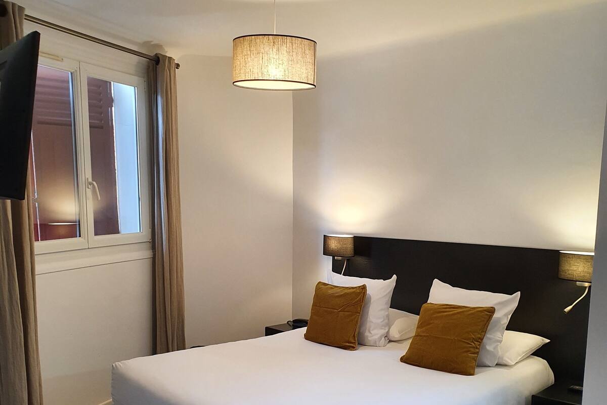 A neatly made bed with white and brown pillows, a black headboard, and a hanging lamp above.