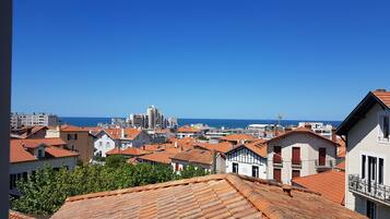 Un paysage urbain côtier avec des bâtiments aux toits de tuiles rouges, un ciel bleu dégagé et une vue sur la mer.