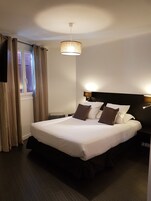 Una cama bien hecha con sábanas blancas y almohadas marrones, una lámpara colgante y una ventana con cortinas.