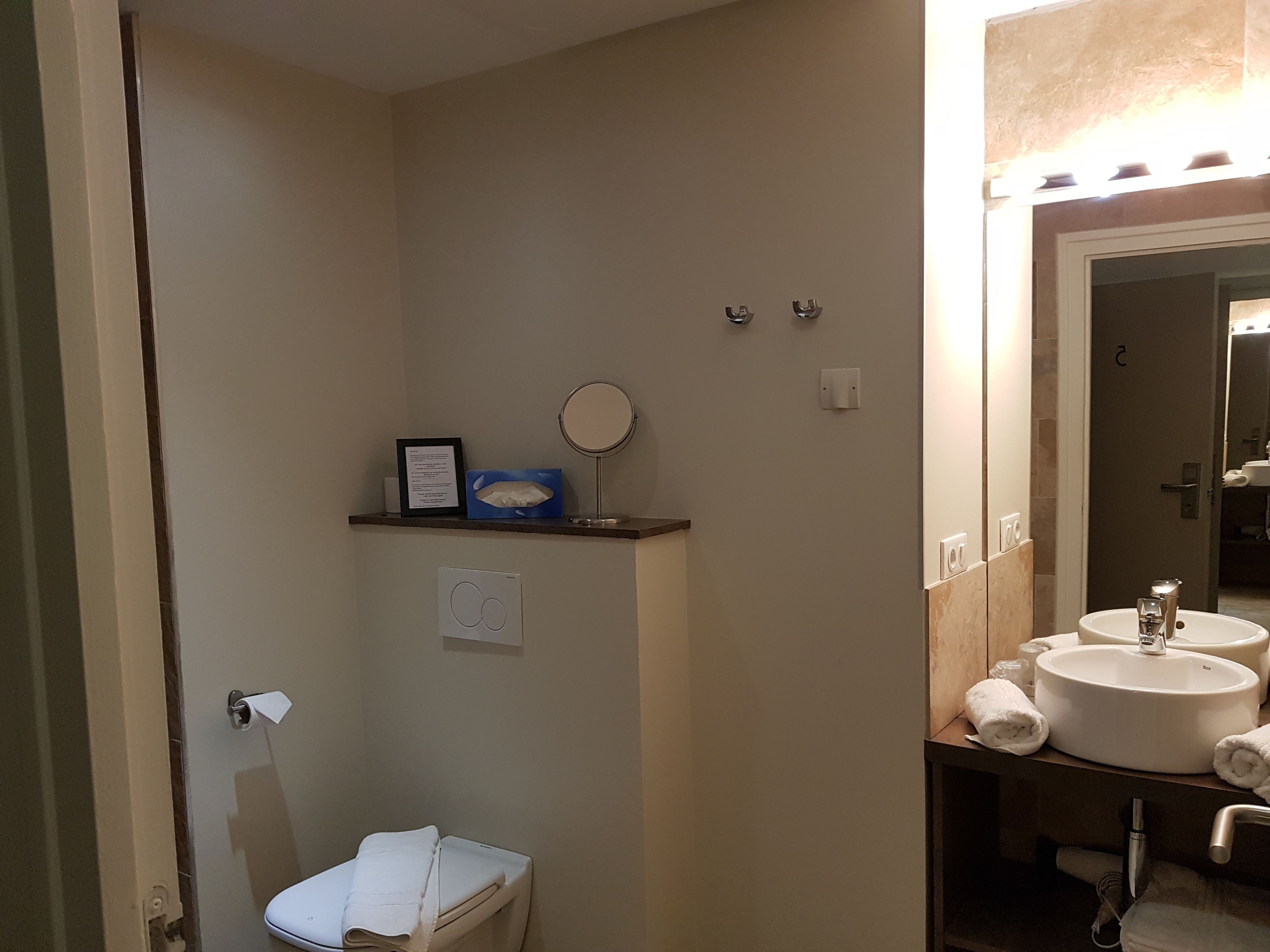 A bathroom with a toilet, a sink, a mirror, and a shelf with a tissue box and a framed note.