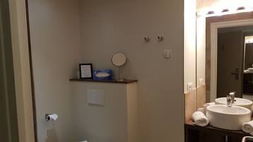 A bathroom with a toilet, a sink, a mirror, and a shelf with a tissue box and a framed note.