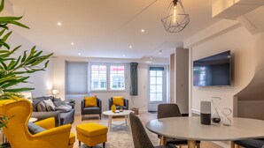 A modern living room with a sofa, armchairs, a dining table, and a TV. - Hôtel Au Bon Coin (Biarritz)
