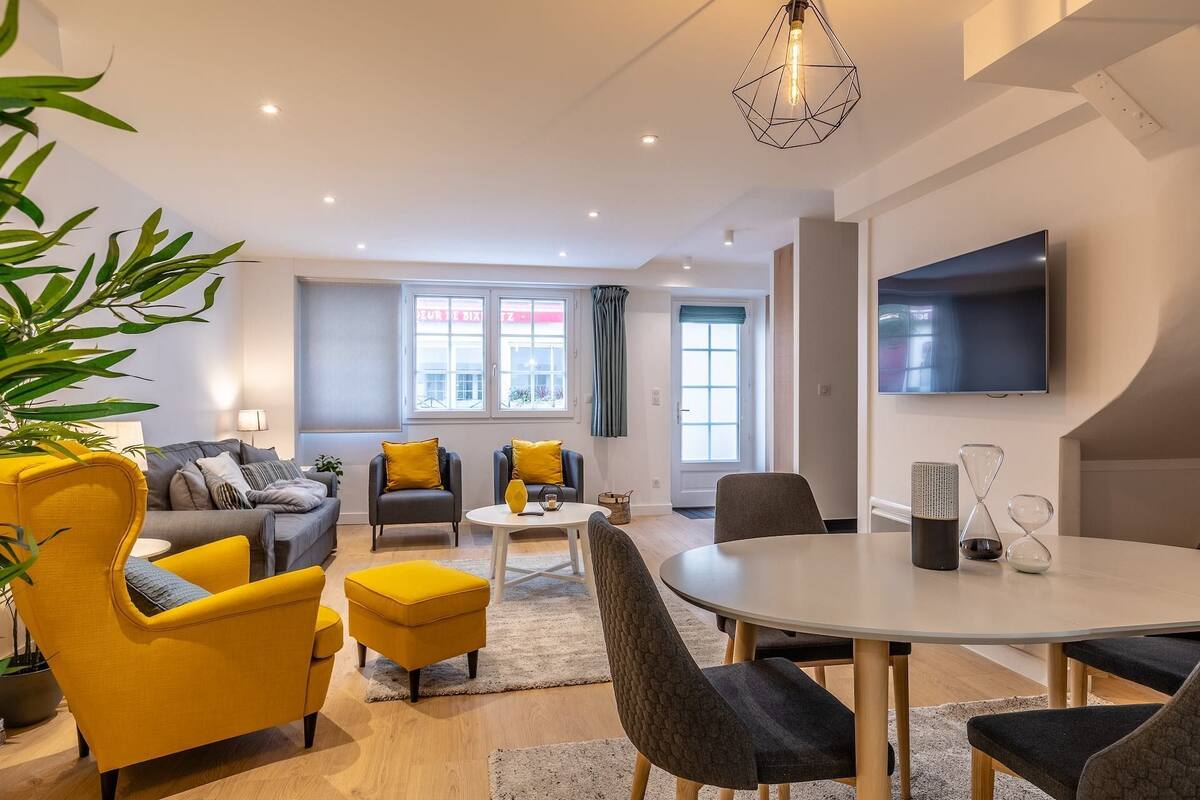 A modern living room with a sofa, armchairs, a dining table, and a TV.