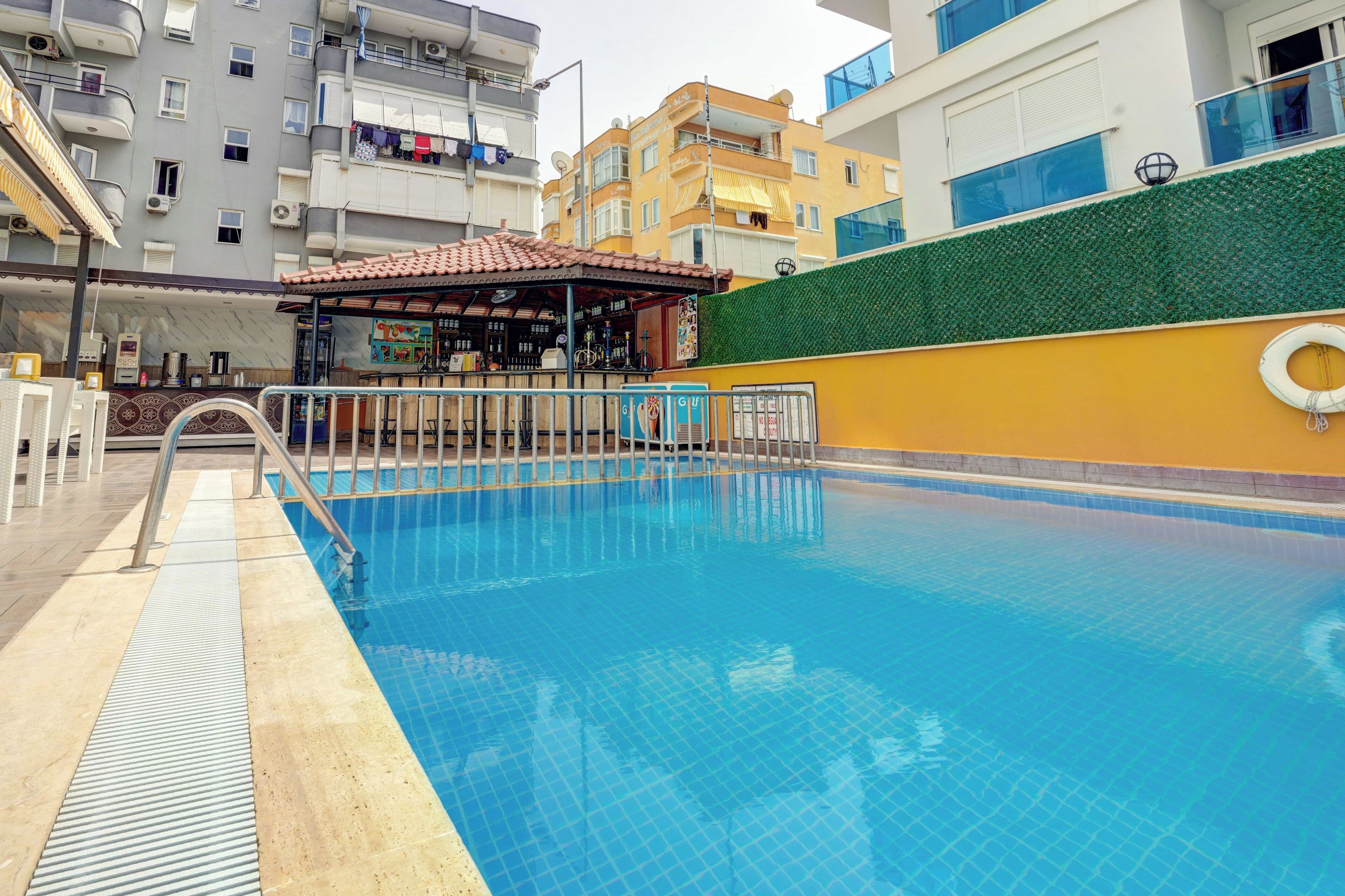 Una piscina con deck de baldosas, una pequeña zona de bar y un muro verde.