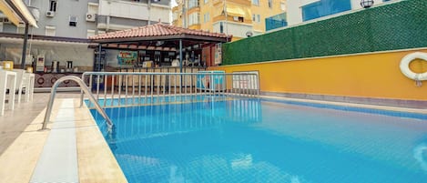Una piscina con deck de baldosas, una pequeña zona de bar y un muro verde.