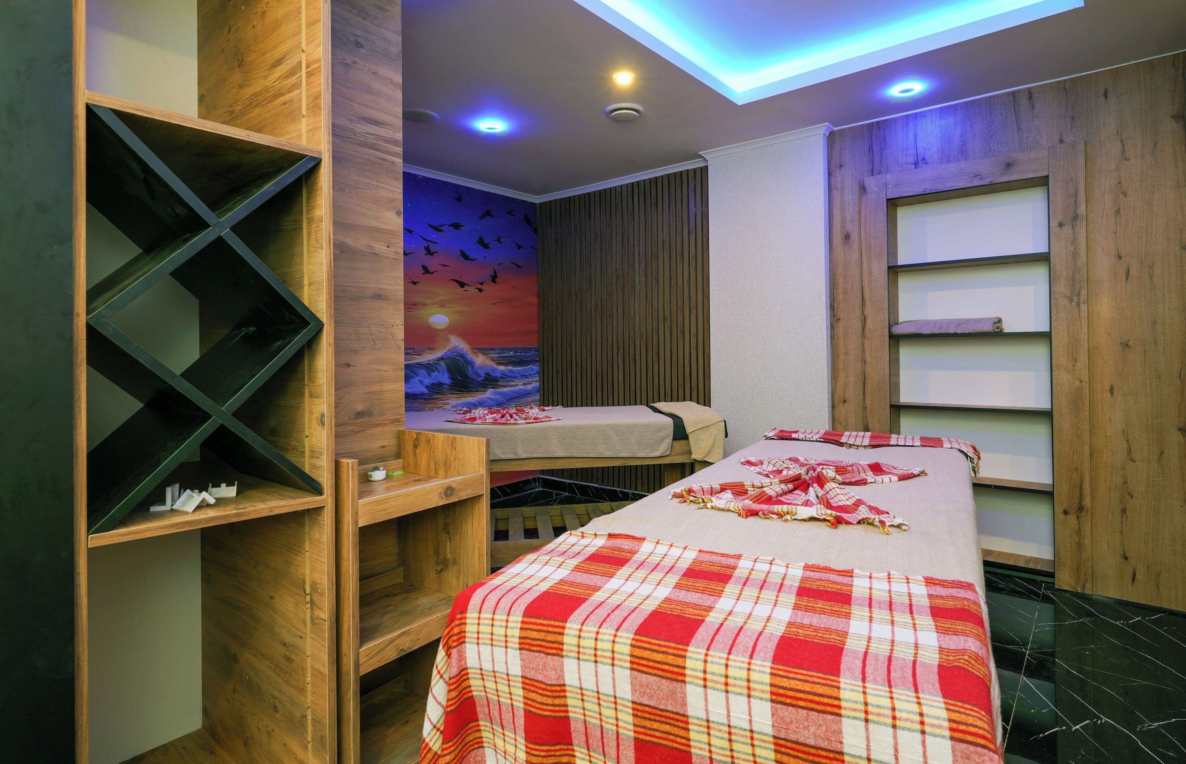 Una habitación con una cama, una repisa de madera, un mural y una lámpara en el techo.