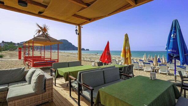 A beachside restaurant with outdoor seating, tables, and umbrellas. - Kleopatra Arsi Hotel (Alanya)
