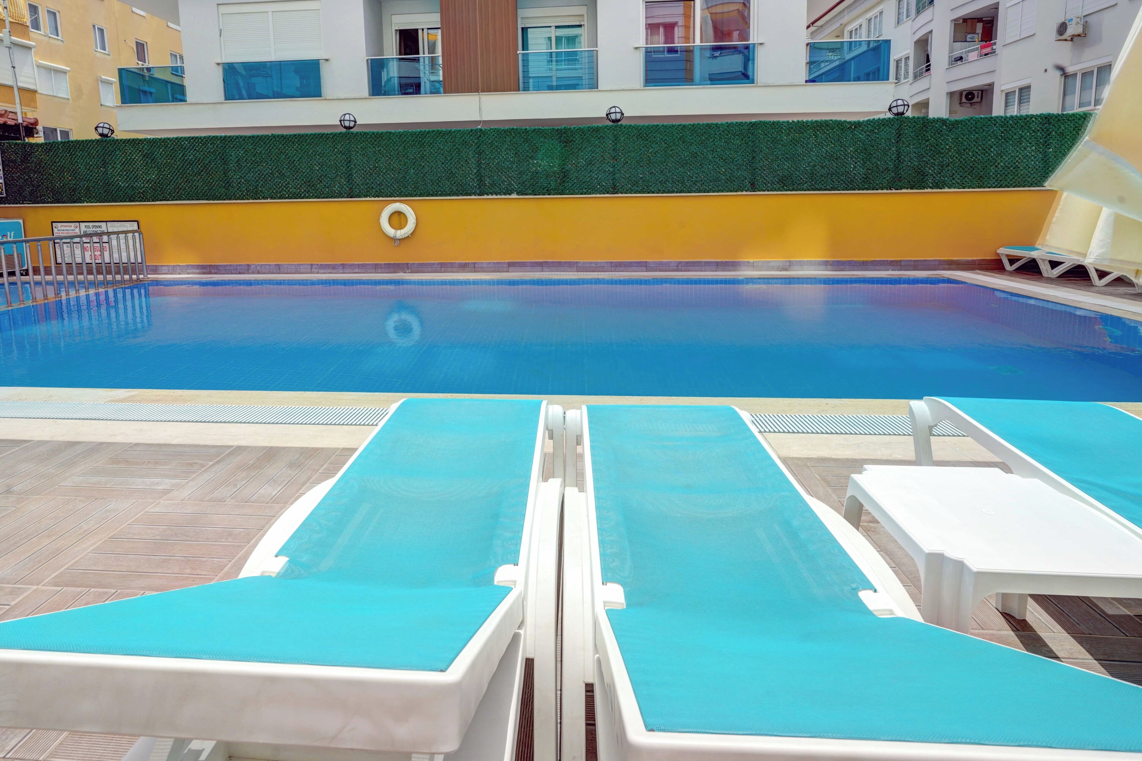 A swimming pool with blue water, surrounded by lounge chairs and a wooden deck.