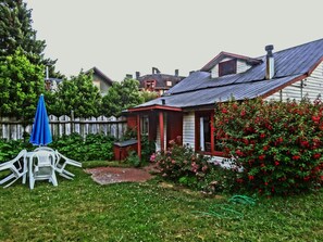 A house with a red and white exterior, a small porch, and a garden with red flowers and green shrubs. - Hostal La Maison (Pucón)