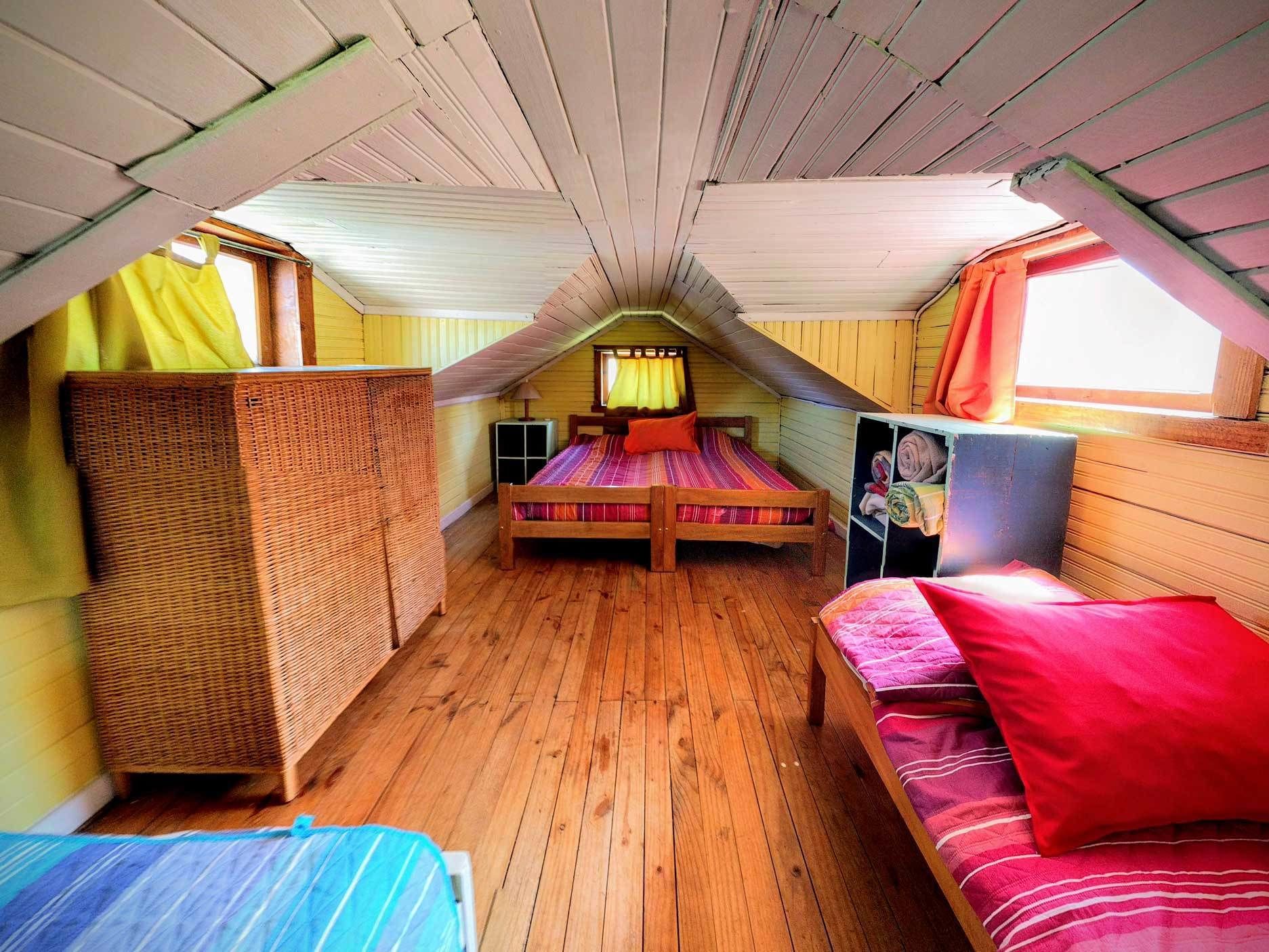Un dormitorio acogedor en el ático con dos camas, un ventanal grande y piso de madera.
