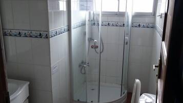A bathroom with a glass-enclosed shower, a toilet, and a sink.