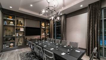 A modern conference room with a long table, chairs, a chandelier, and a large window with curtains.