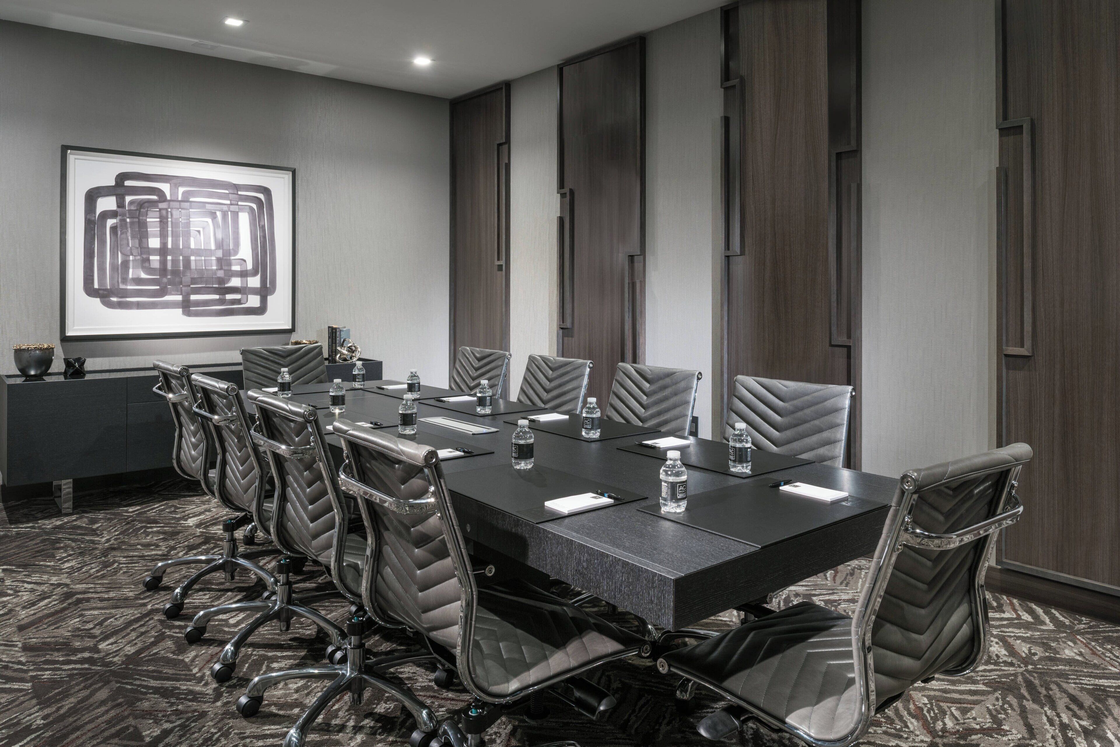 Sala de conferência com uma mesa comprida, várias cadeiras e uma tela de projetor exibindo uma imagem abstrata.