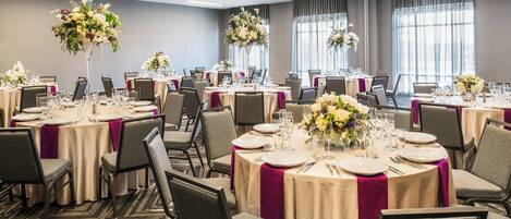 A banquet hall with round tables, chairs, and floral centerpieces.
