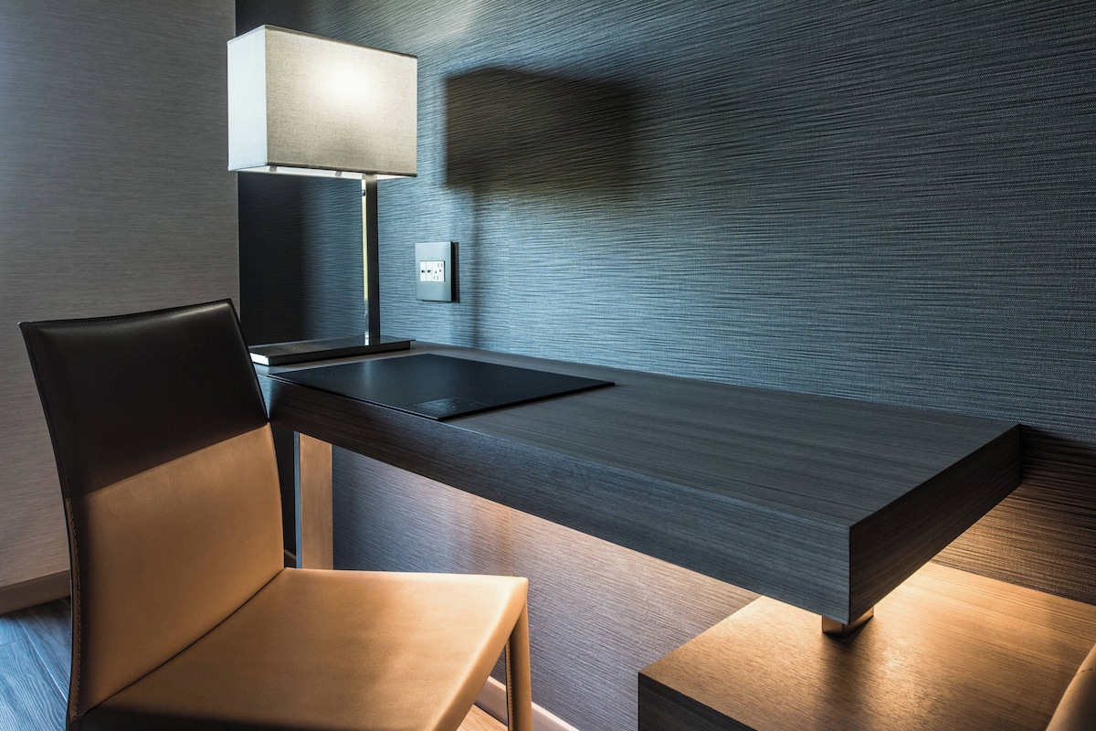 A modern room with a dark wooden desk, a black chair, and a lamp.