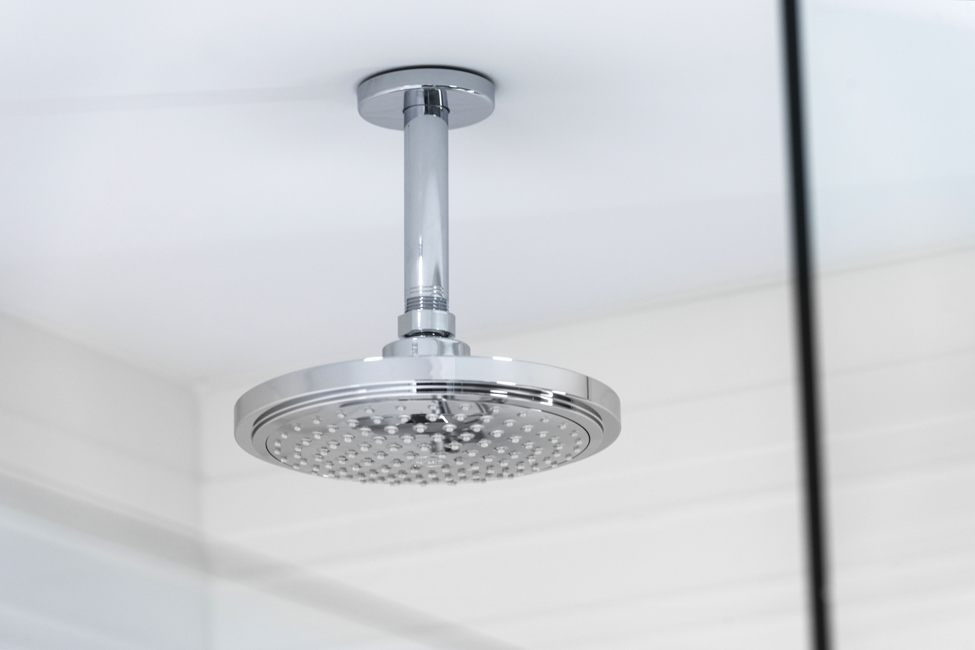 A modern showerhead with a chrome finish, mounted on a ceiling with a white background.