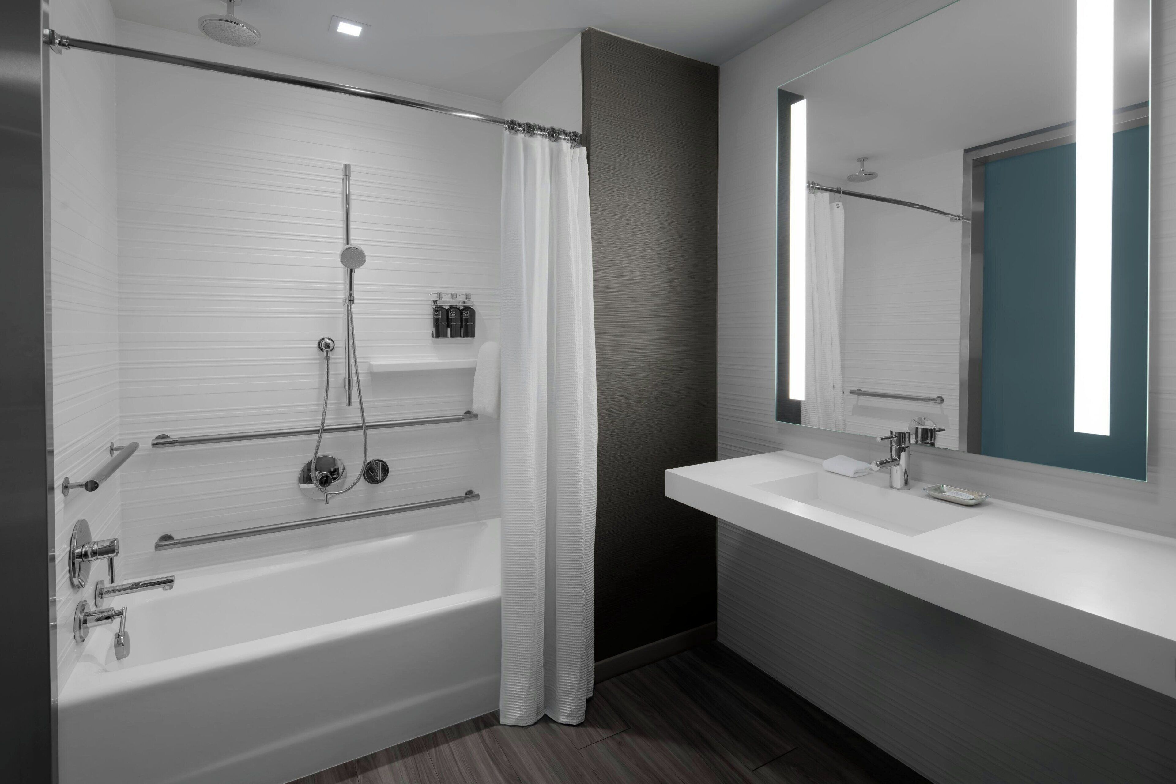 A modern bathroom with a bathtub, shower, and a large mirror.