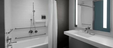A modern bathroom with a bathtub, shower, and a large mirror.