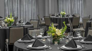 Un comedor formal con mesas redondas dispuestas para varios invitados, con manteles negros, platos blancos y servilletas negras.