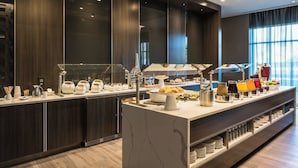 A modern breakfast buffet with a marble island, glass display cases, and a variety of food and drink options.