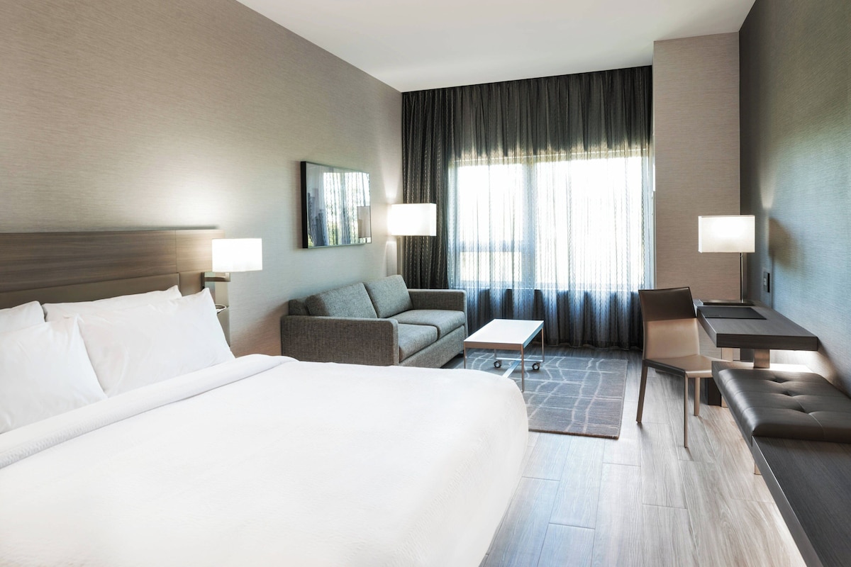 A hotel room with a large bed, a sofa, a small table, a chair, and a desk.