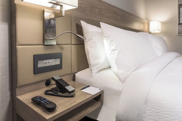 A hotel room with a bed, bedside table, phone, and a wall-mounted light fixture.