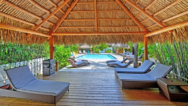 A covered outdoor area with a pool, lounge chairs, and a wooden deck. - Siesta Key Palms Resort (Sarasota)