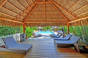 A covered outdoor area with a pool, lounge chairs, and a wooden deck. - Siesta Key Palms Resort (Sarasota)