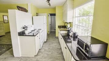 A kitchen with white appliances, a microwave, and a window with blinds.