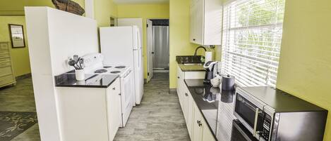 A kitchen with white appliances, a microwave, and a window with blinds.